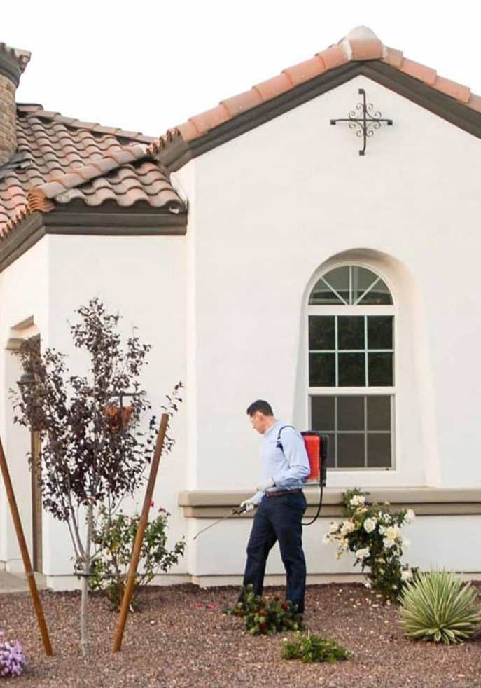 T2 Pest control technician treating the exterior of a home.